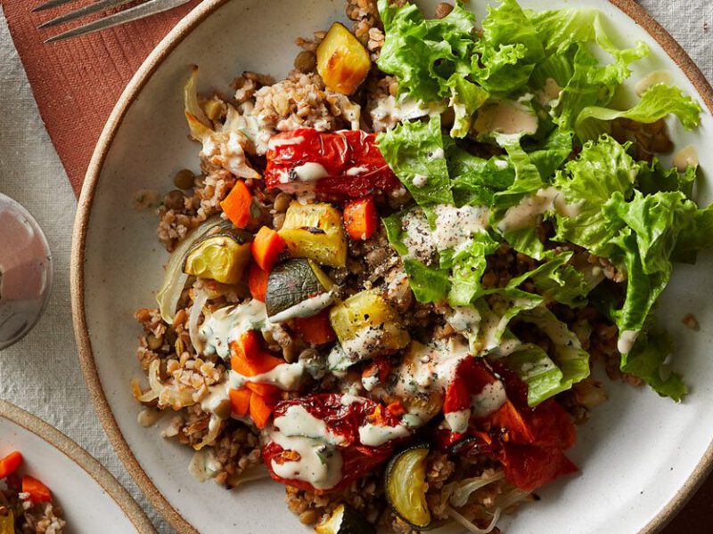vegan mujadara bowls with chopped lettuce, colorful vegetable medley, lentils, and a creamy homemade tahini sauce with parsley - shown in a white bowl in sunlight