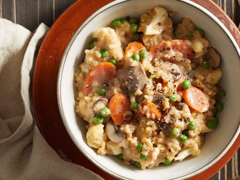 creamy vegan risotto with mushrooms, carrots, and peas, in a white bowl on a red plate