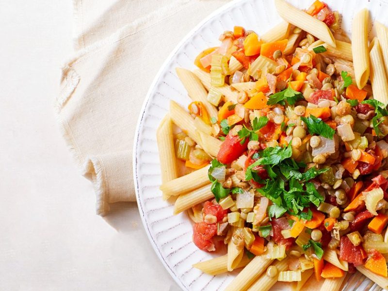 Hearty Lentil Ragu with Penne on a white plate with a metal fork