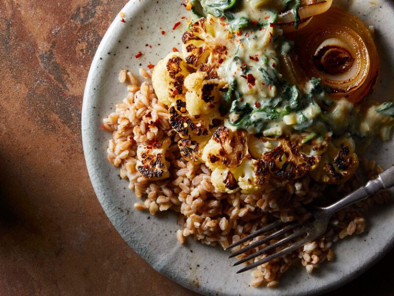 Roasted Cauliflower Steaks with Creamed Spinach on a white plate with a metal fork