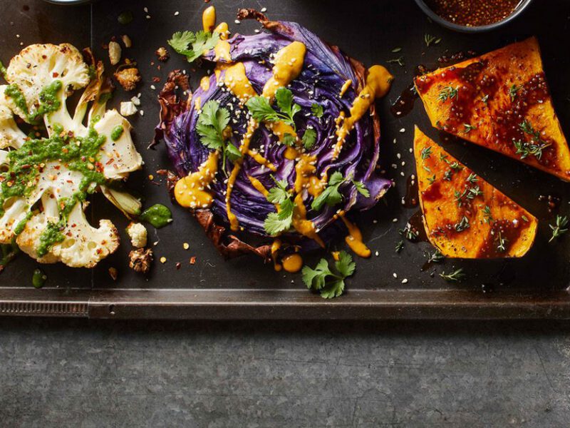 Three slices of grilled veggie steaks, one cauliflower, one cabbage, one cauliflower, drizzled with sauce