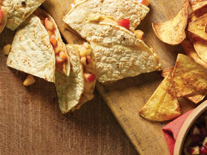 Cinnamon Apple Quesadillas on a wooden cutting board next to a bowl of apple salsa
