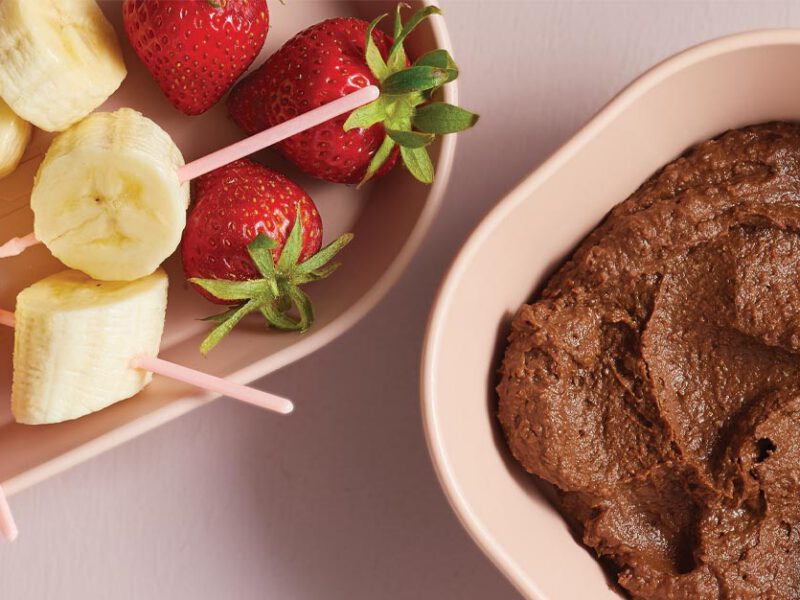 Healthy Chocolate Hummus in a light pink bowl next to a plate of fresh fruit slices