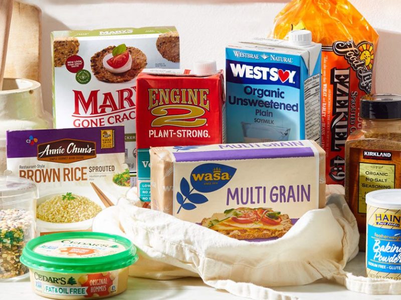 An array of oil-free vegan food products found at the grocery store, spread out on a kitchen counter, for whole-food, plant-based shoppers