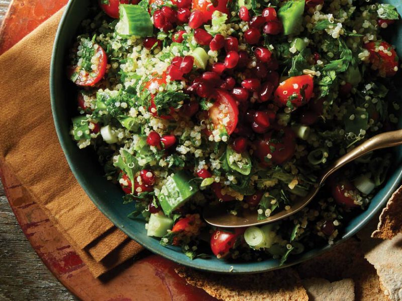 Quinoa Tabbouleh with Pomegranate Seeds in a blue dish with a gold metal spoon and a side of crackers