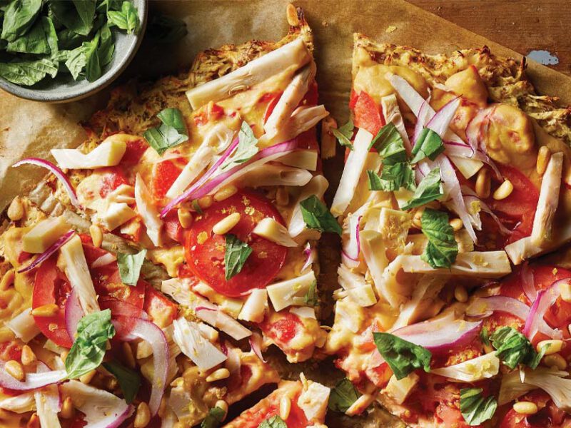Parsnip-Crust Veggie Flatbread on parchment paper next to a small bowl of basil leaves