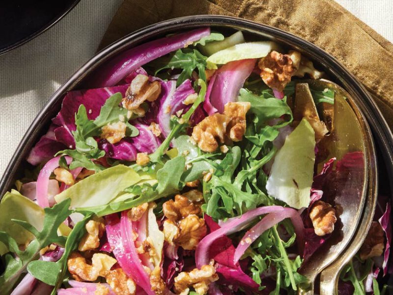 Tricolor Salad with Quick-Pickled Onions on an oval serving platter with gold metal serving spoons