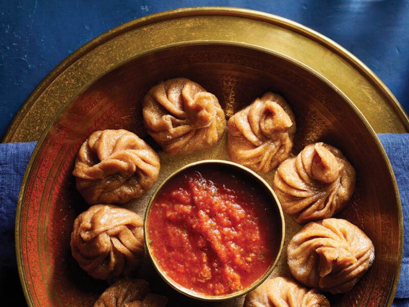 Tofu Vegetable Momos with Tomato Chutney on a gold metal plate on a dark blue tabletop