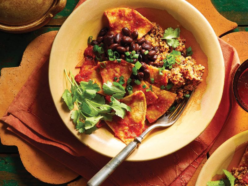 Vegan Chilaquiles in a cream colored bowl with a form set on an orange napkin against a green table