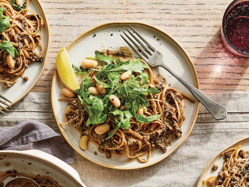 Linguine with Mushroom Pesto topped with arugula on white ceramic plates against a wood tabletop