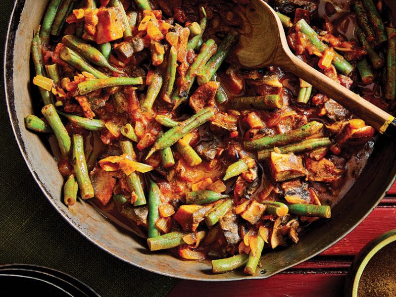 Inguday Tibs (Spicy Ethiopian Mushrooms) in a large metla pot with a wooden spoon against a red wooden background