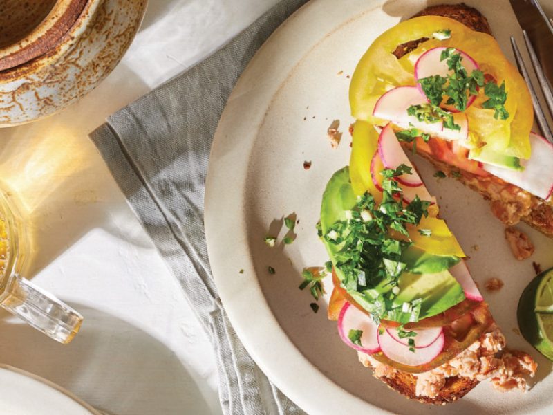 Avocado Toast with Tomato and Spicy Gremolata cut in half on a white plate with a silver knife and fork on the side