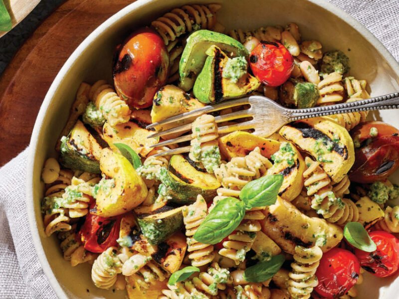 Basil-Leek Pesto Pasta with Cherry Tomatoes and Summer Squash in a white bowl on a cloth napkin in a wooden plate