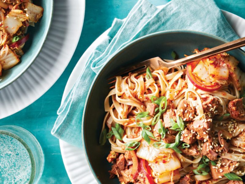 Vegan Bulgogi Noodles with Jackfruit Kimchi in a blue ceramic bowl on a pale blue napkin on a white plate with a fork sitting in the dish