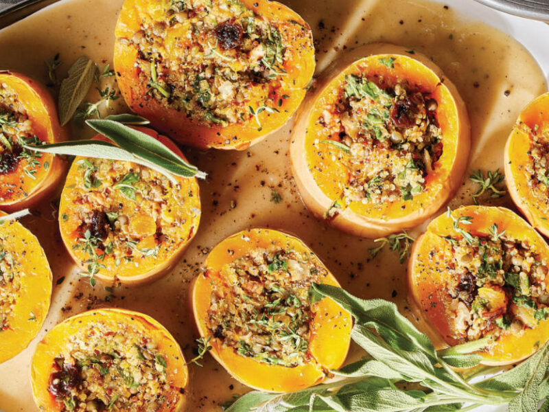 Quinoa-Stuffed Butternut Squash with Arugula, Pecans, and a Savory Gravy on a platter garnished with fresh sage leaves