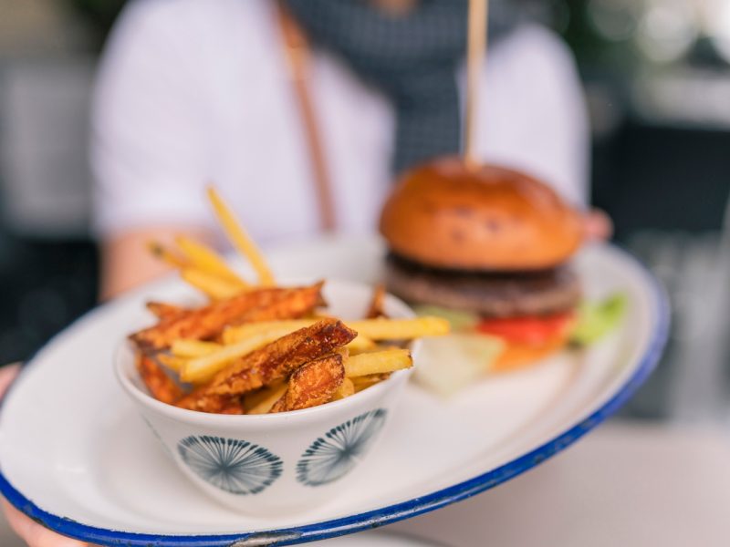 person holding out burger and deep-fried french fries on a plate