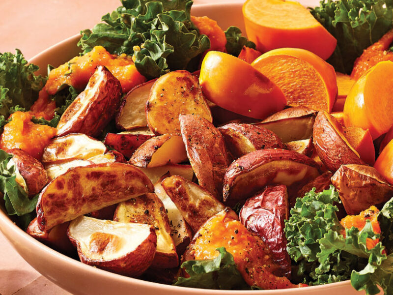 Warm Roasted Potato, Kale, and Persimmon Salad in a peach bowl on a peach counter