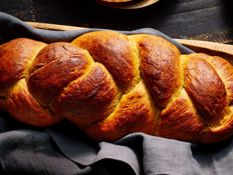 Vegan Challah Bread in a long wooden bowl on top of a blue linen towel