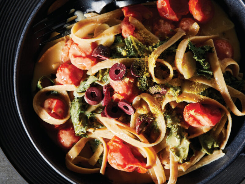 Creamy Baked Fettuccine with Kale in a black serving bowl on a black plate with a black cloth napkin
