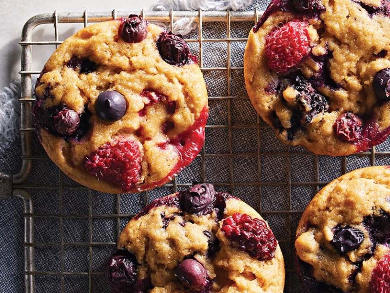 Five fresh-baked Triple Berry Muffins on a wire cooling rack