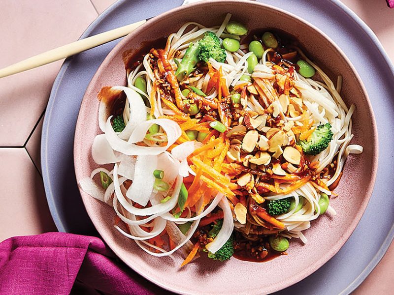 A wide-rimmed, pale pink bowl of 30-Minute Spring Roll Bowl with daikon ribbons and colorful veggies