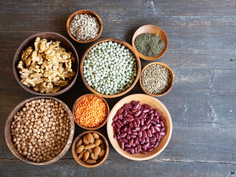 A collection of small and medium size bowls, each filled with legumes or nuts, on a wooden gray background