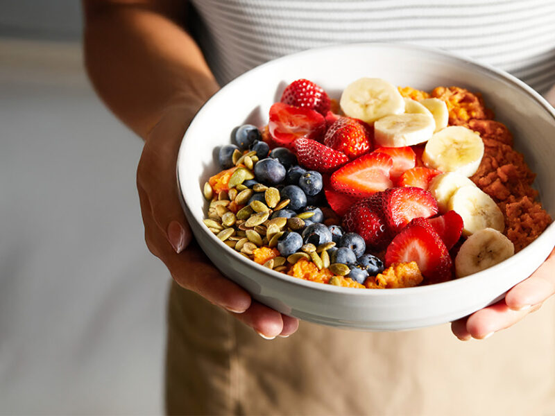 A woman holding a Rainbow Sweet Potato Breakfast Bowl with two hands