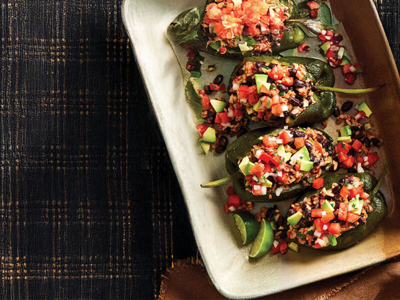 Four Chipotle Black Bean and Rice Stuffed Poblanos in a casserole dish resting on a black checkered cloth