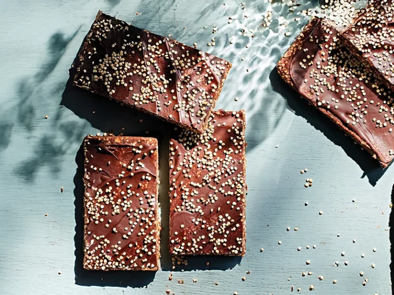 Six No-Bake Chocolate-Oat Energy Bars on a pale blue background, with grains of uncooked quinoa scattered around