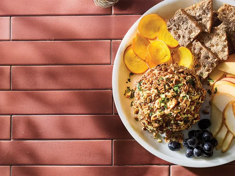 Cranberry Hummus Vegan Cheese Ball on a plate with whole grain crackers, sliced pears, and graps