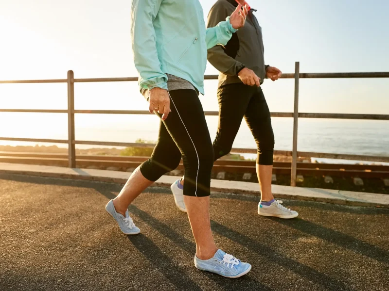 Two women shown from the shoulders down wearing windbreakers and leggings and sneakers, walking on a boardwalk