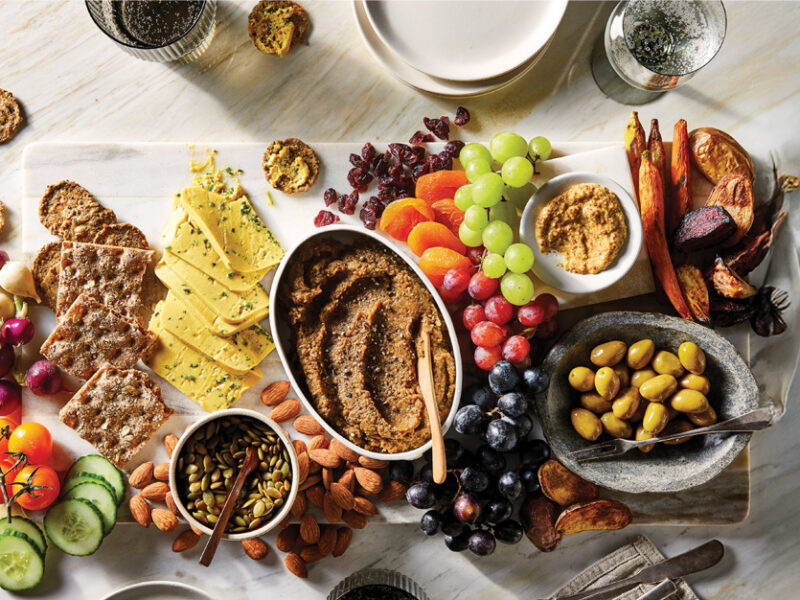 A vegan charcuterie board featuring grapes, olives, nuts, dried fruit, a homemade vegan pate and homemade vegan cheese, and toast