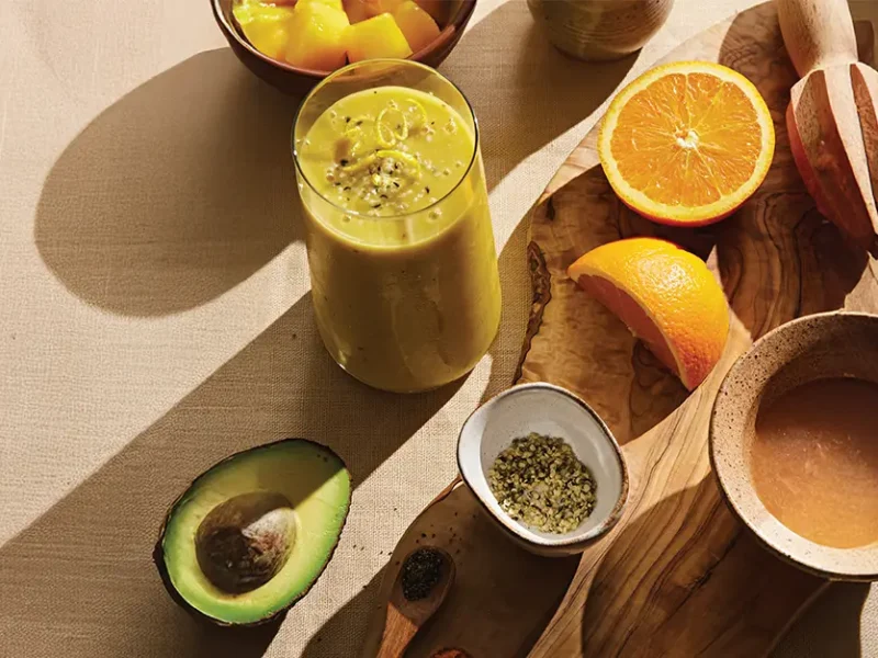 Power Citrus Smoothie next to a chopping board, cut oranges, half an avocado. The sun is streaming in from the side