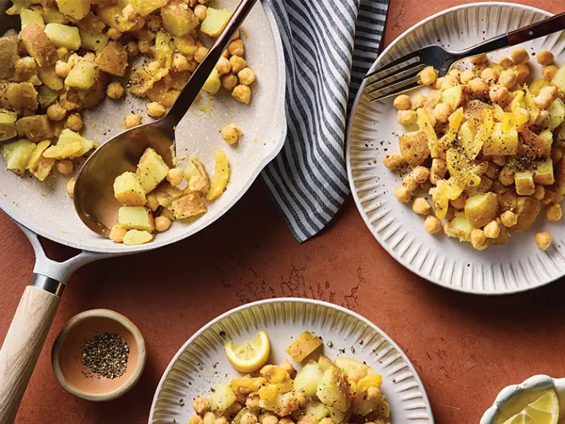 A non-stick skillet of Quick Curried Chickpeas and Potatoes, with some dished up onto two plates