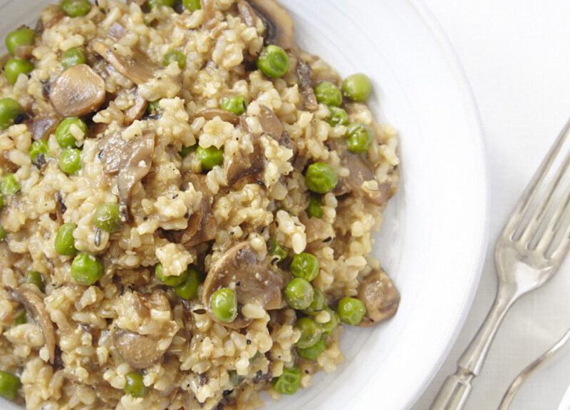 Top-down view of Mushroom and Green Pea Risotto on a white plate on a white background