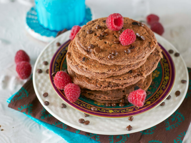 A stack of Chocolate Buttermilk Pancakes topped with vegan chocolate chips and fresh raspberries