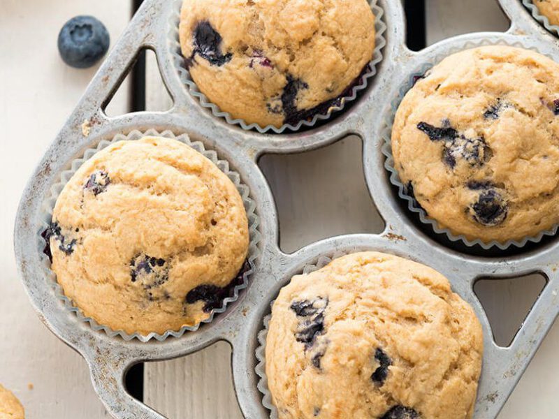 A muffin tray of Whole-Wheat Berry Muffins with three muffins to the side