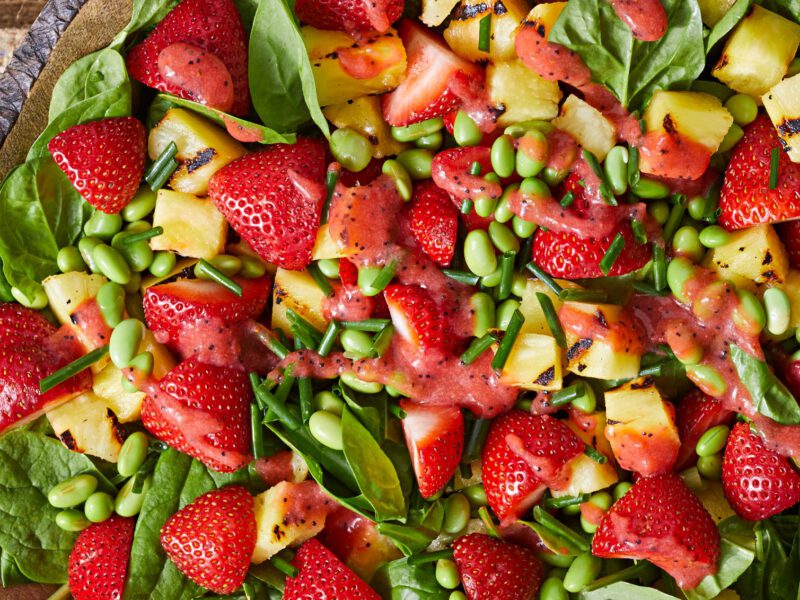 Spinach, Pineapple, and Strawberry Salad in a rustic homemade ceramic bowl on a piece of hessian