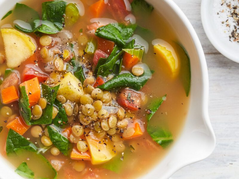 Mediterranean Lentil and Spinach Soup in a white bowl next to a pinch bowl of cracked black pepper
