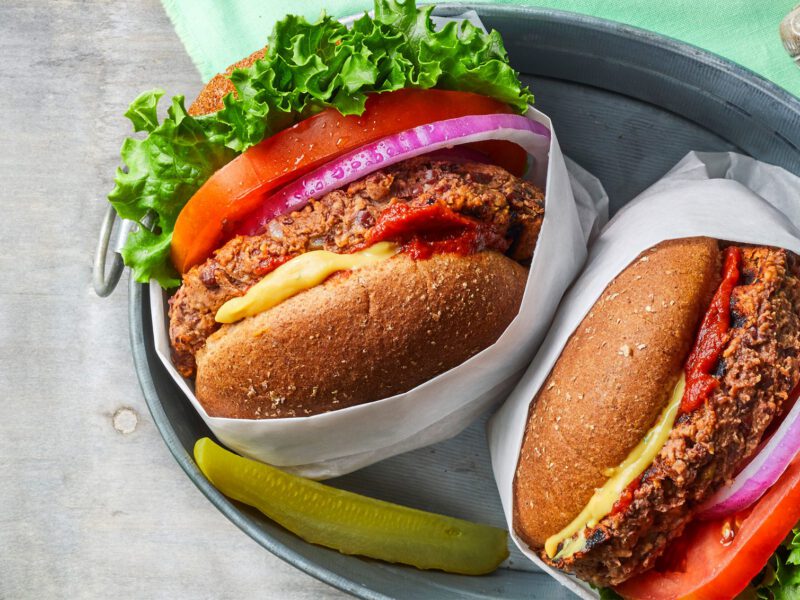 Two vegan five-ingredient veggie burgers with homemade patties and vegan cheese and slices of onion and tomato, shown from the side, in wrappers